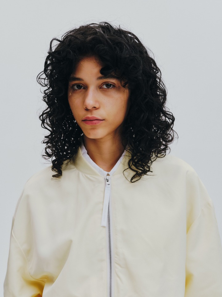 リブ仕様の襟とドロップショルダー、ジッパー付きポケットで実用性とミニマルな印象を両立